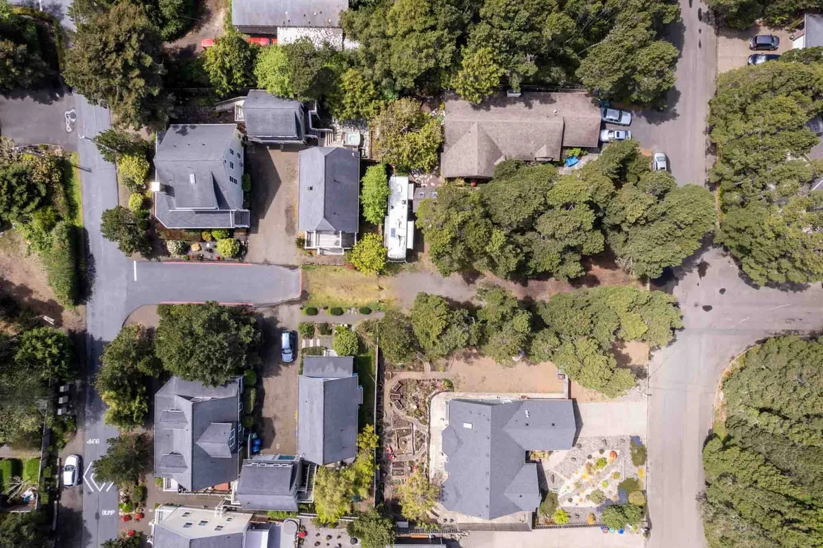 A serene view of the neighborhood featuring residential houses, lush green trees, neatly arranged gardens, and driveways. The scene reflects a peaceful, family-oriented community ideal for children to play and neighbors to connect.