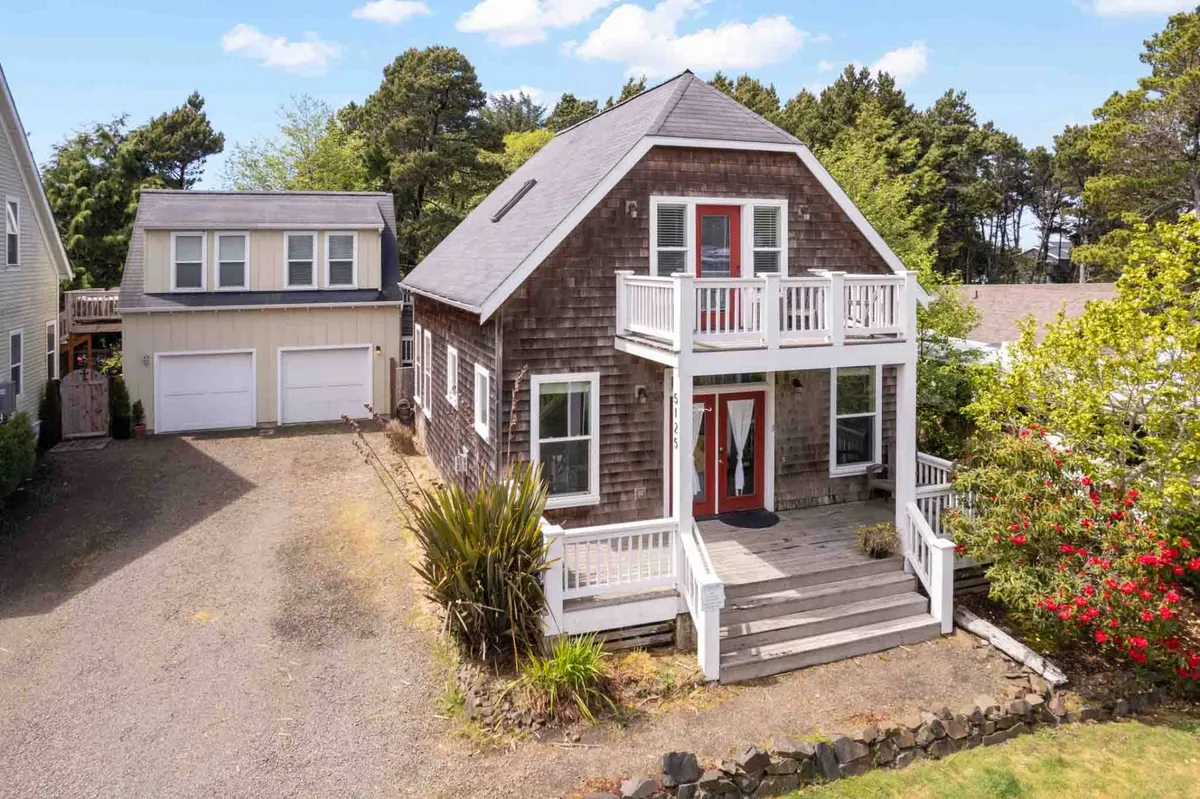A welcoming front porch scene with red doors, thoughtfully arranged landscaping, and comfortable seating. The area is bathed in natural light, suggesting a peaceful spot to enjoy morning coffee or relax with a gentle sea breeze.