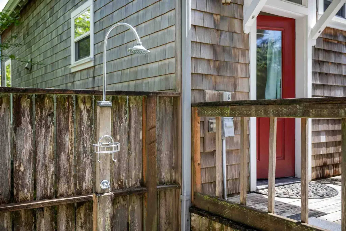 A bright outdoor shower area with a red door and textured wooden fence, set just off the deck. The open-air setting emphasizes fresh air and a seamless transition from beach days to home, perfect for rinsing off sandy toes.
