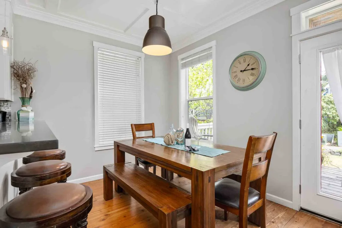 A close-up of a stylish dining area, featuring a large table set beneath a pendant light and surrounded by windows. The scene radiates warmth and is set for a shared meal or morning coffee, with natural light streaming in to create a welcoming environment.