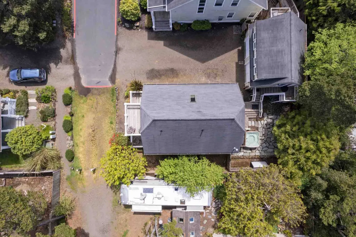 An outdoor area with visible house roofs, a driveway, surrounding vegetation, and a patio space. The setting is tranquil and ideal for gatherings or relaxed supervision of children at play.