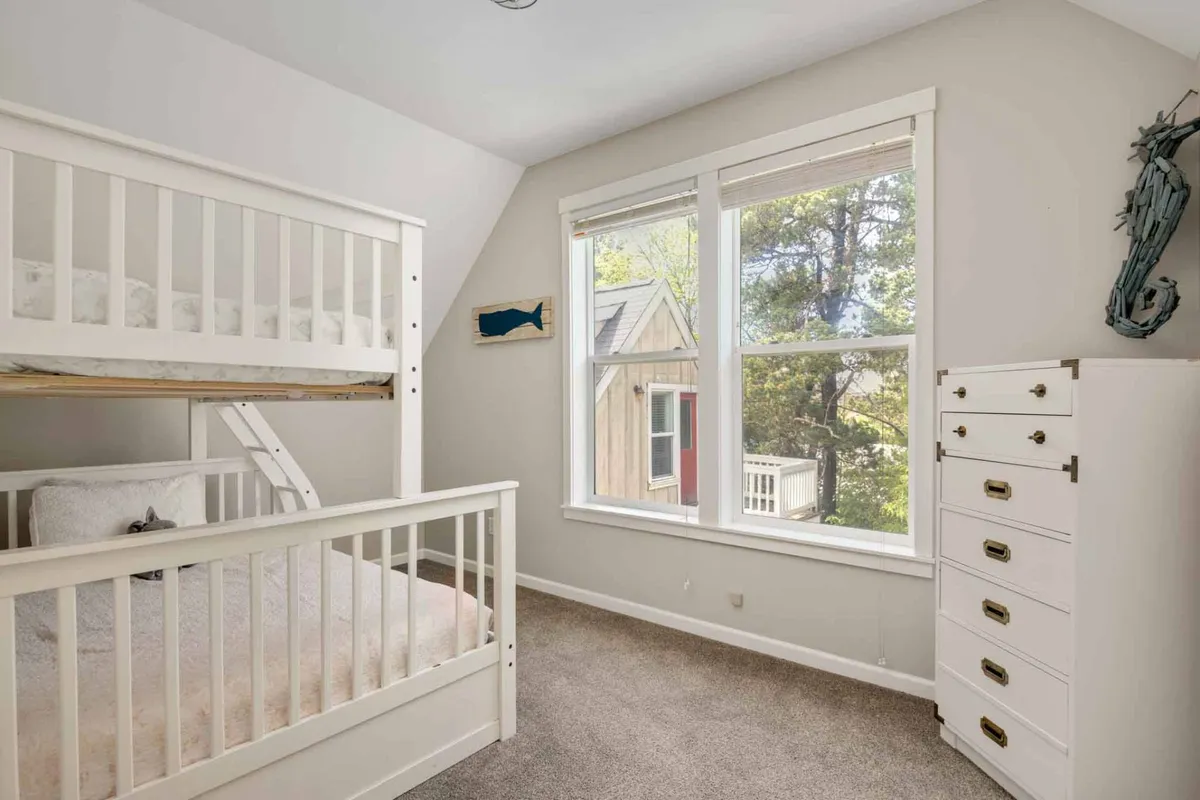A cozy children's bedroom featuring a bunk bed, a window with views to the outside, and a dresser. The space appears playful and inviting, suggesting a comfortable spot for kids to relax or play indoors after enjoying community amenities.