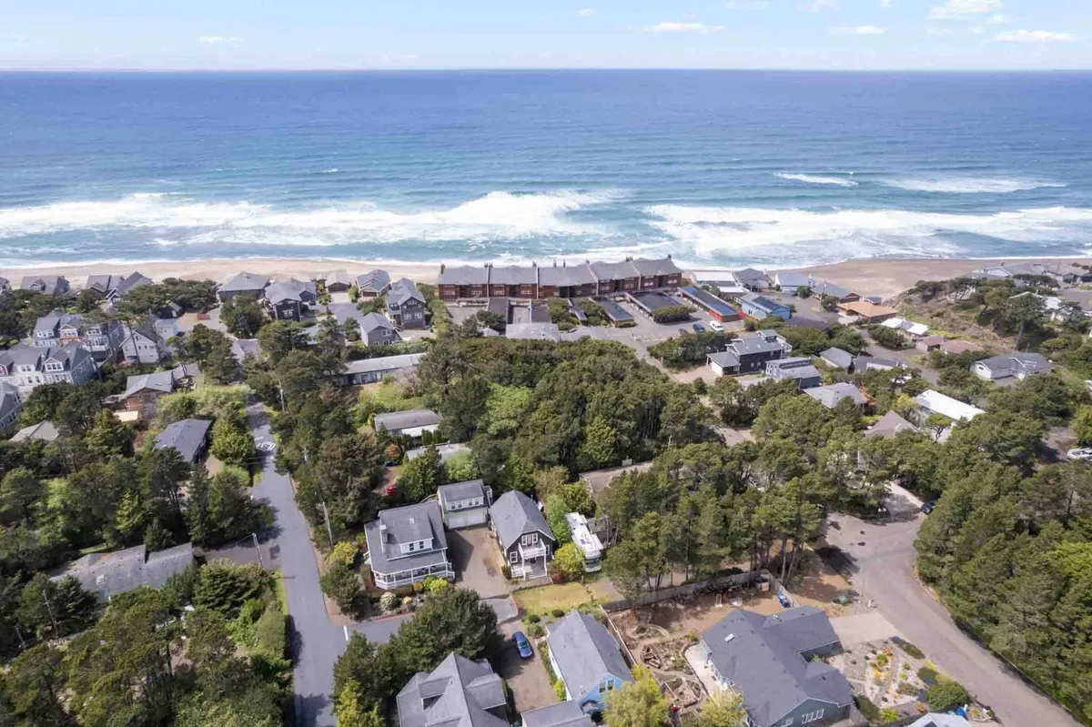 A sweeping view of the coastline with ocean waves rolling in, coastal homes nestled among trees, and community roadways. The image captures the proximity of the beach, sense of neighborhood, and accessible community amenities.